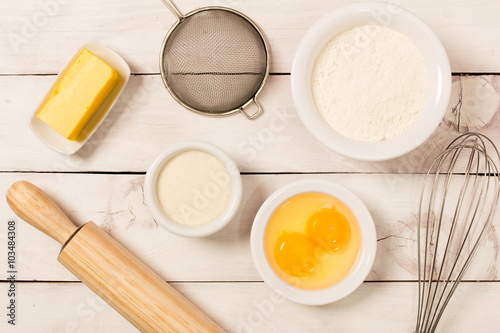 Baking in rustic kitchen recipe ingredients (eggs, flour, milk, butter) on white  wooden table from above. 