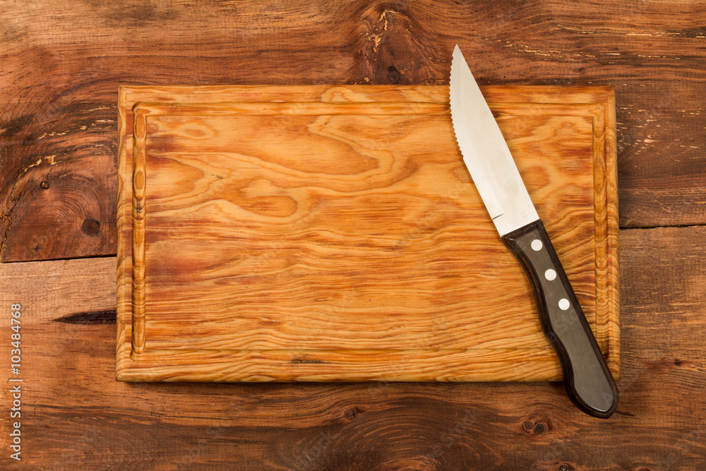 Chopping board, with a meat knife on wooden background 