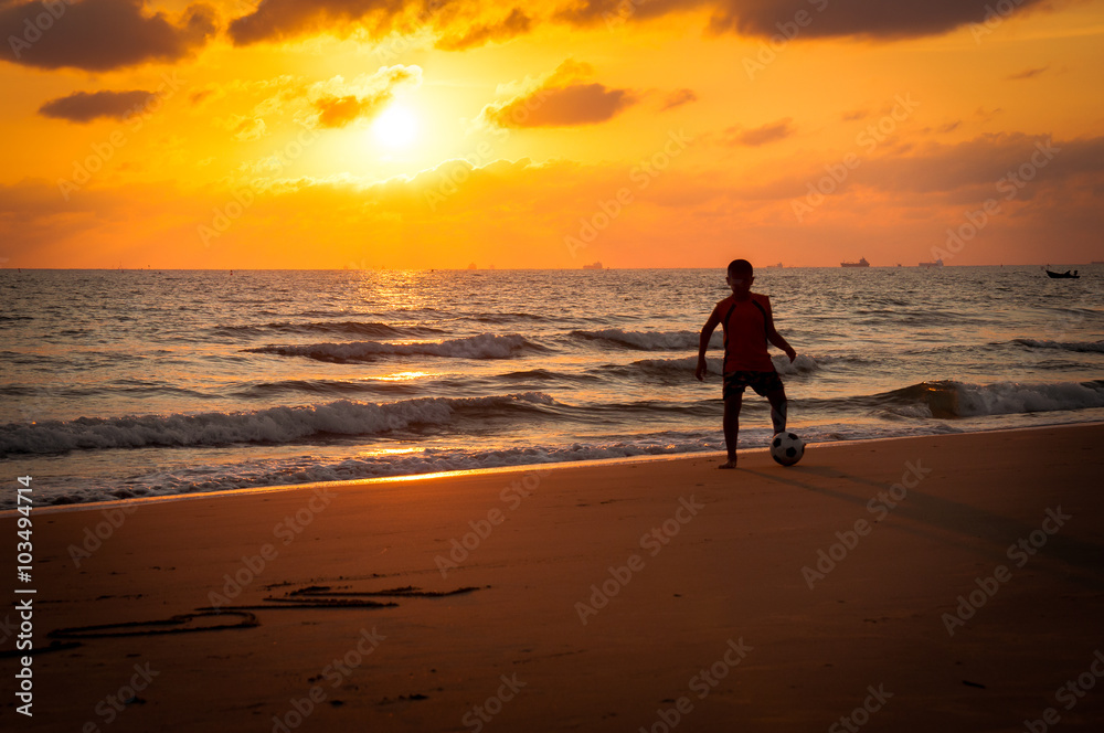 Silhouette of young boy playing a football on the beach in sunse Silhouette of young boy playing a football on the beach in sunse