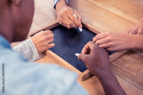 Cropped hands of business people writing on slate at desk