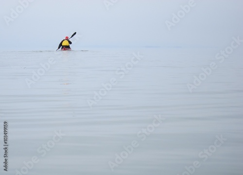 Man in red kayak and yellow jacket on the calm blue lake in early spring