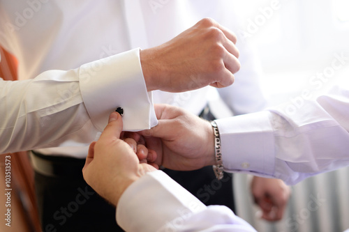 Groomsmen helping the groom with his cufflinks