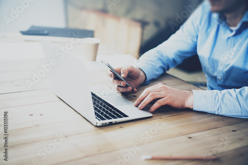 Businessman typing message smartphone. Generic design laptop on the table. Working hard new project. Blurred background, horizontal mockup.