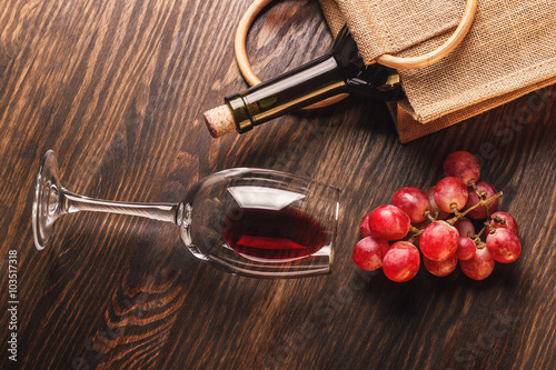 Glass with wine, a bottle and bunch of grapes, wooden background