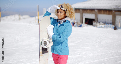 Attractive young woman posing at a winter ski resort in her ski clothes holding her snowboard and smiling at the camera  with copy space