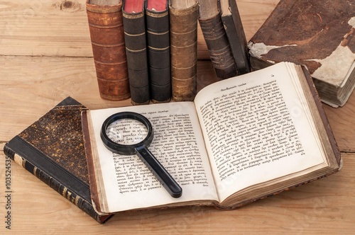 Tableau sur toile Antiquarian open book and magnifying glass on the table