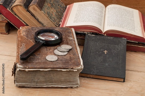 Antiquarian books, magnifying glass and silver coins on the table