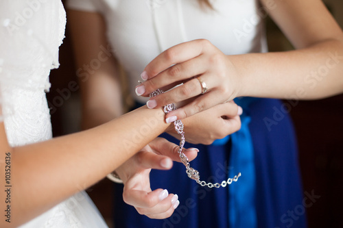 beautiful elegant bridesmaid putting on bracelet on the bride's