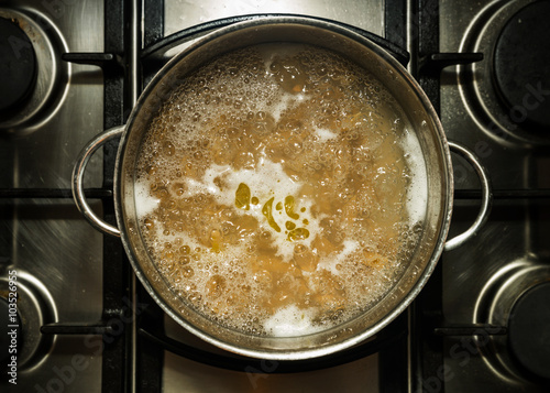 Metal cooking pan with boiling water and wholewheat penne pasta on a stove photo