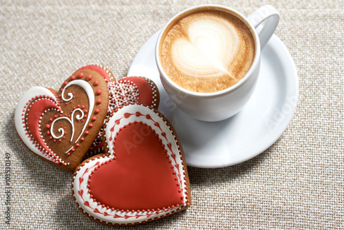 Lovely decoration. Top view shot of a cup of coffee decorated with froth art and heart shaped cookies on the coffee shop table