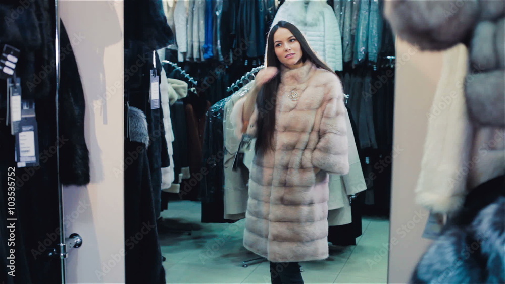 Beautiful brown-haired girl chooses a fur coat in the store. Shopping. Series. Beautiful brown-haired girl chooses a fur coat in the store. Shopping. Series.