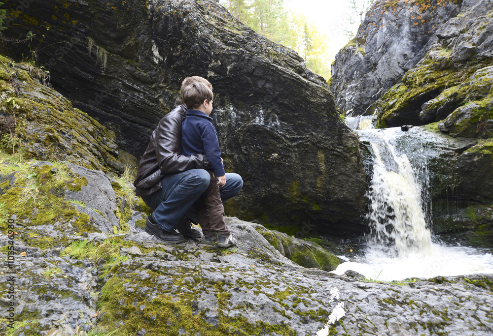 father and son on the rocky bank of a forest stream