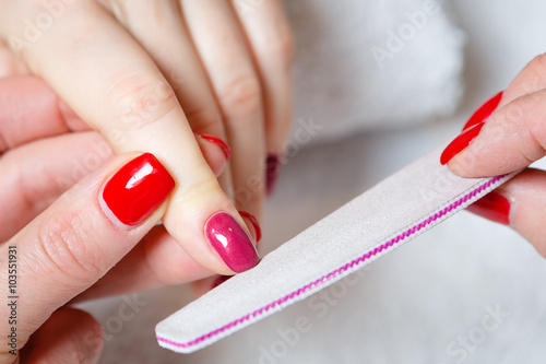 Closeup shot of a woman in a nail salon receiving a manicure by a beautician with nail file. Woman getting nail manicure. photo