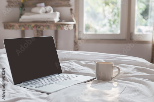 Coffee cup and laptop on the bed in morning time