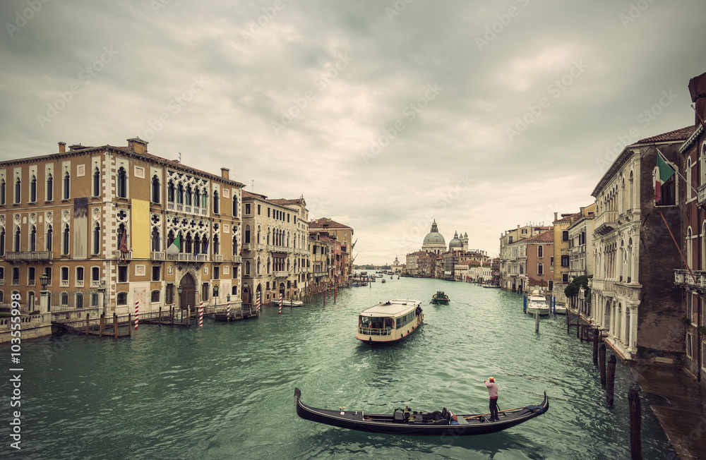 View of traditional Gondola and boats on Canal Grande with Basilica di Santa Maria della Salute church in background at a cloudy day, Venice (Venezia), Italy, Europe, Vintage filtered style
