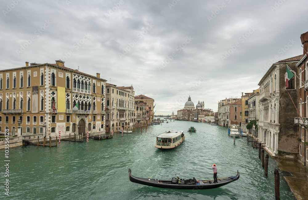 Beautiful view of traditional Gondola and boats on Canal Grande with Basilica di Santa Maria della Salute church in background at a cloudy day, Venice (Venezia), Italy, Europe
