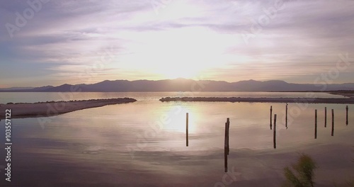 Over Water Towards Sunset / 4K footage of a drone flying from the bay towards the sunset/sunrise on a cloudy day over a stoney pier with birds flying around.