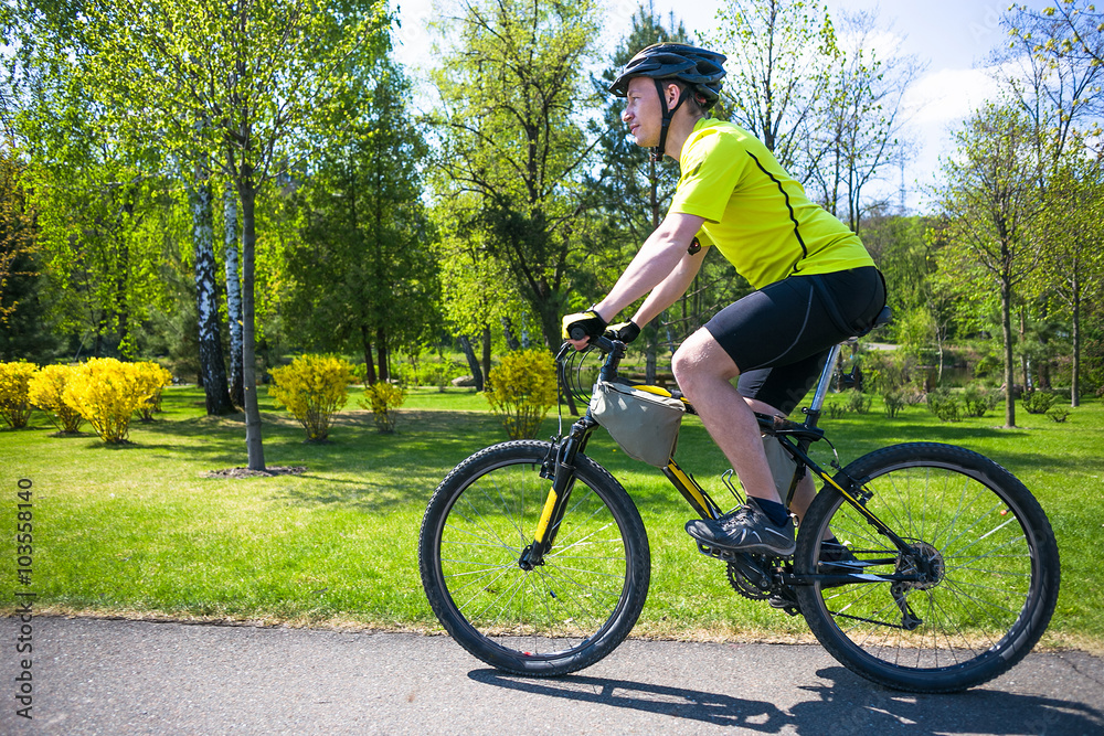 Naklejka premium Bicyclist rides on the road in city park. Sunny summer hot day