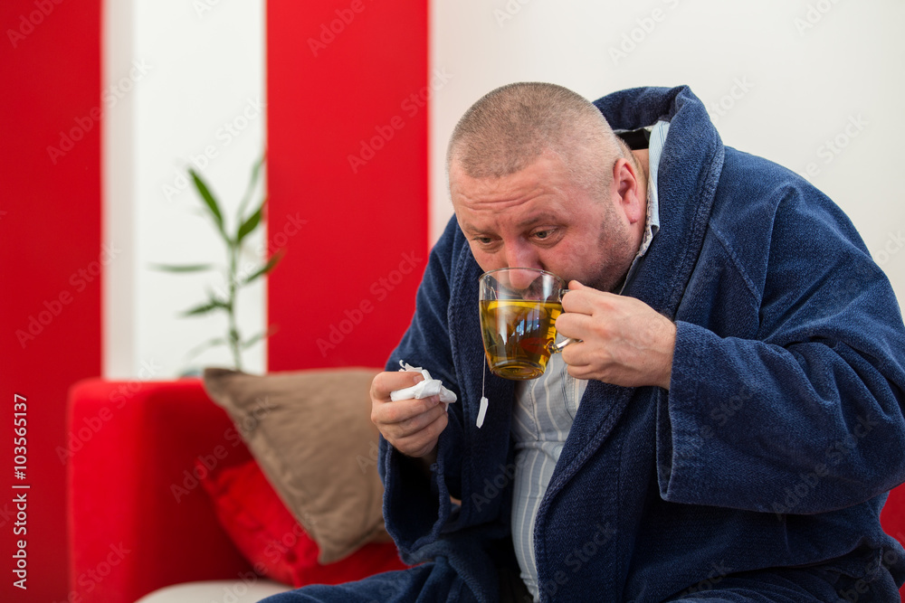Ill man blowing his nose with paper napkin and drinking tea at home Ill man blowing his nose with paper napkin and drinking tea at home