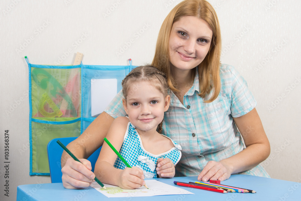 Five-year girl and young mother together paint a picture on a sheet of paper Five-year girl and young mother together paint a picture on a sheet of paper