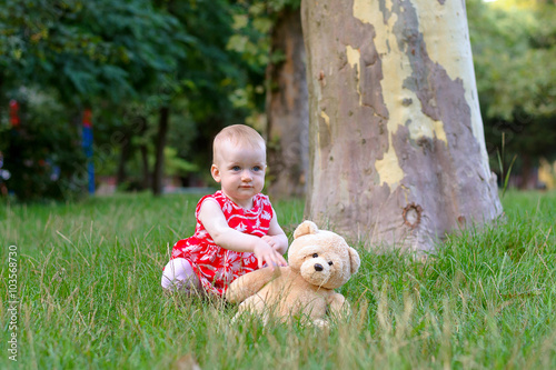 a girl plays with a teddy bear in a park on a grass photo