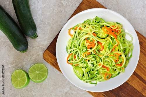 Fotografie Low carb zucchini noodle dish with carrots and lime on white marble background,