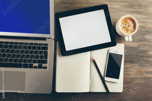 Modern laptop, mobile phone, tablet, notebook and coffee cup on wooden table