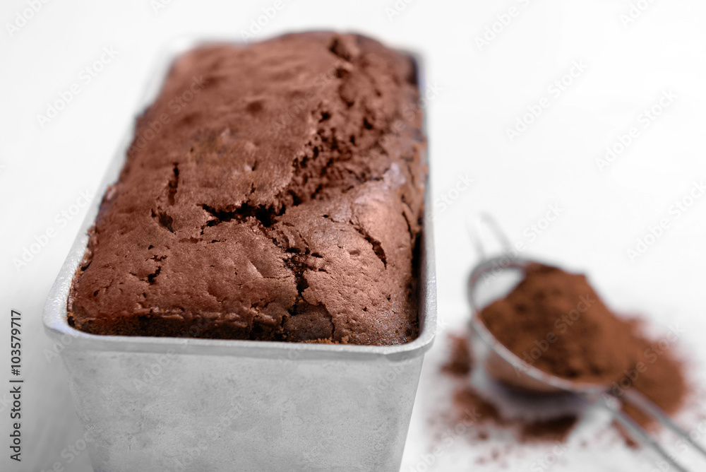 Chocolate cake in baking dish with cocoa powder on white table Chocolate cake in baking dish with cocoa powder on white table