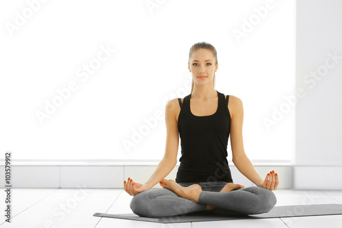 Health concept. Young attractive woman does yoga exercise in the gym against white wall