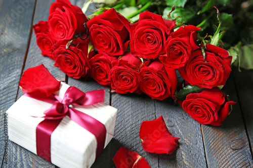 Bouquet of fresh red roses and present box on wooden background