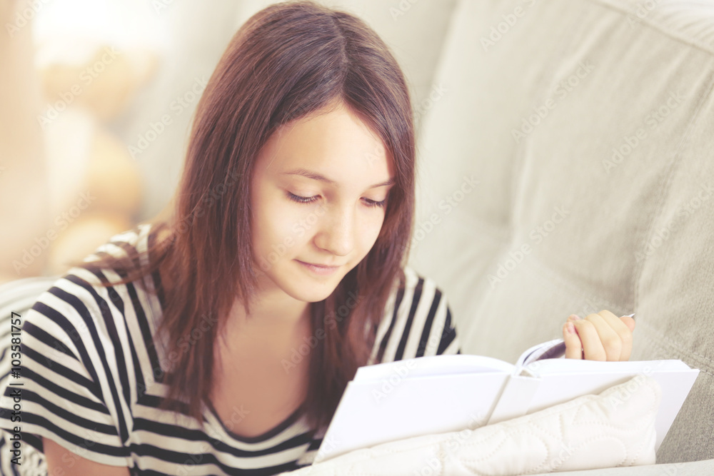 Beautiful girl reading book on sofa, indoor Beautiful girl reading book on sofa, indoor