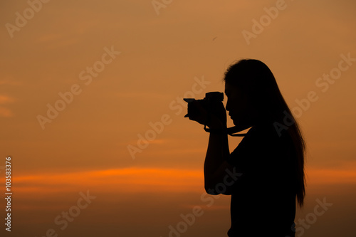 Silhouette of woman shooting with camera at sunset