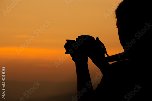 Silhouette of woman shooting with camera at sunset