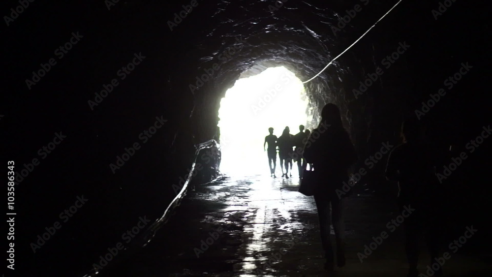 Silhouette of people go through the dark tunnel into the glowing end. Freedom and solution concept