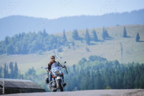 Biker in sunglasses on mountainous road, man is riding his custom made travel motorbike. Sunny day in the mountains. Tilt shift soft effect