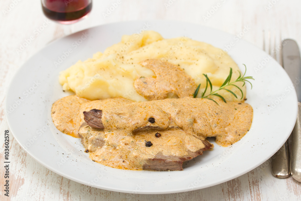 meat with sauce and mashed potato on white plate on brown background