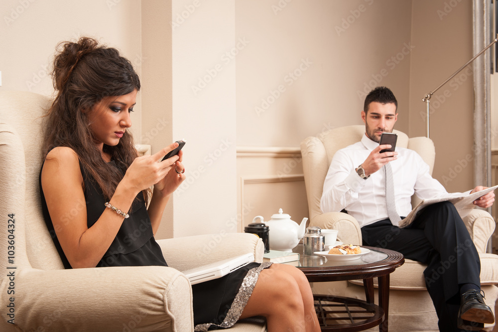 Young couple using smartphone sit on armchairs in luxury hotel. Young couple using smartphone sit on armchairs in luxury hotel.