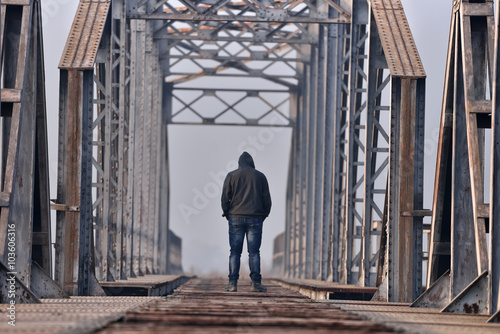 Sad teenager in depression sitting on the bridge at the sunset.
