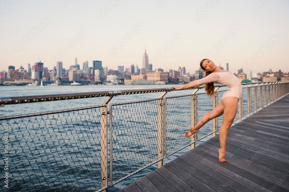 Fototapeta premium Young beautiful ballerina dancing along New Jersey waterfront with New York as background.
