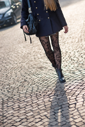Legs detail of young woman wearing lace stockings walking in the street.
