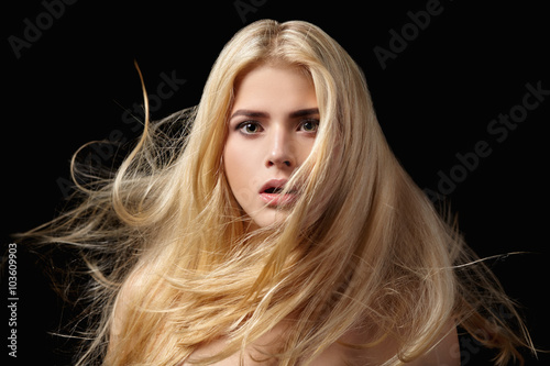 Portrait of blonde girl with flying hair on black background