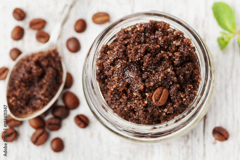 Body scrub of ground coffee, sugar and coconut oil in glass jar on white rustic table, homemade cosmetic for peeling and spa care, top view Body scrub of ground coffee, sugar and coconut oil in glass jar on white rustic table, homemade cosmetic for peeling and spa care, top view