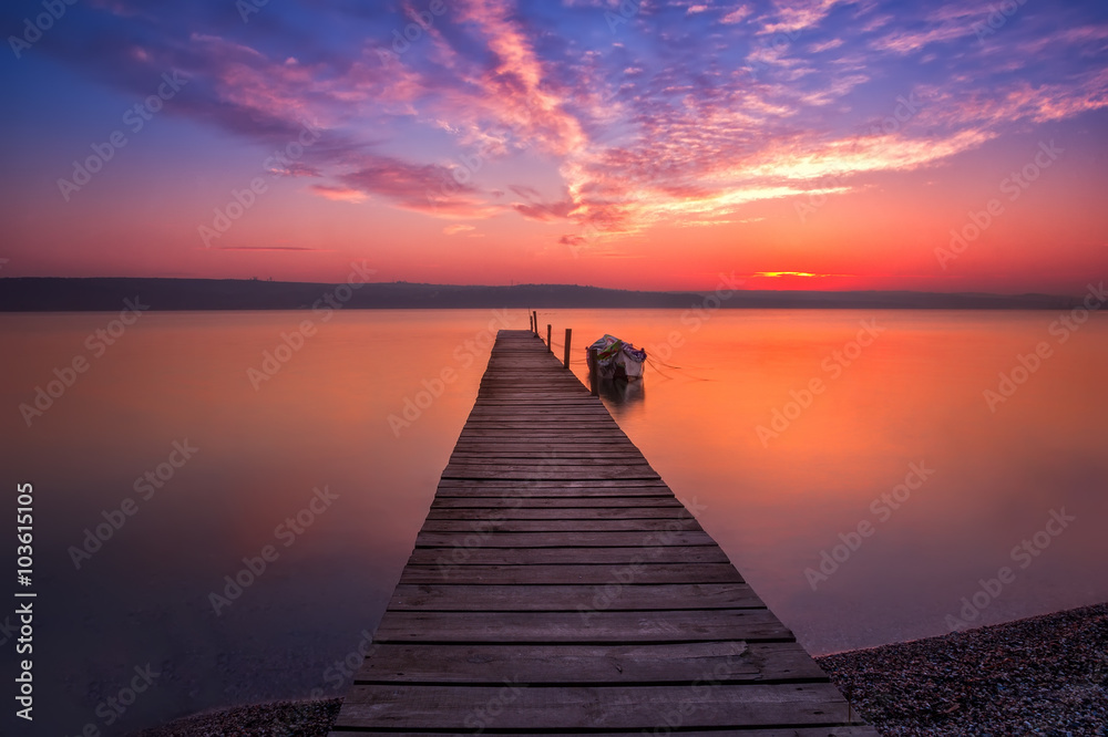 Magnificent long exposure sunset with wooden pier and boat.