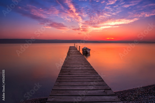 Magnificent long exposure sunset with wooden pier and boat.