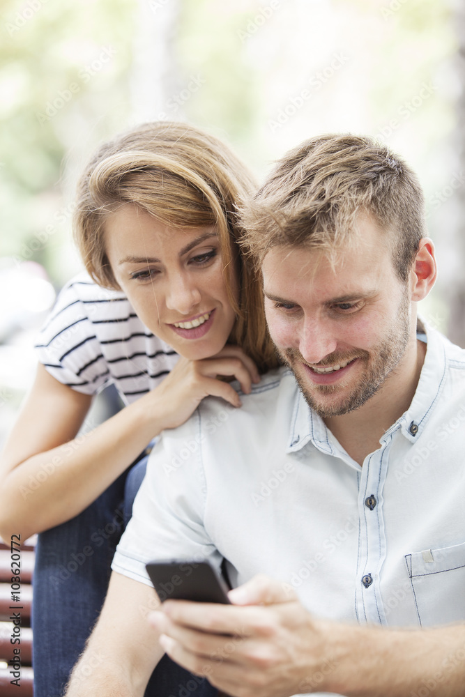 Happy couple with smart phone. Happy young loving couple standing outdoors together and looking at the mobile phone together Happy couple with smart phone. Happy young loving couple standing outdoors together and looking at the mobile phone together