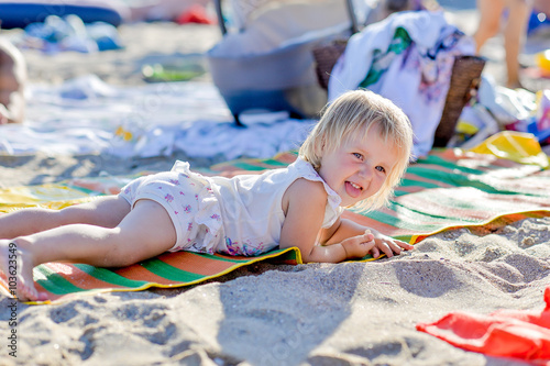 little blond girl is lying on the beach