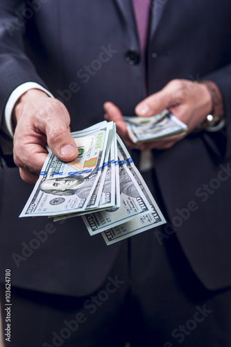 Man in a dark suit holds out hand with money