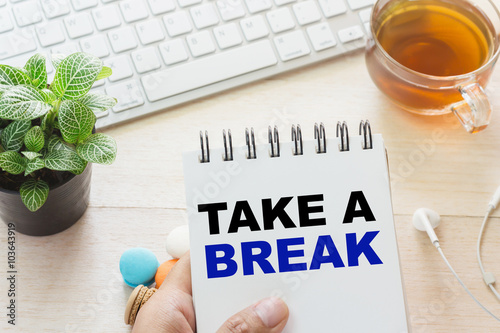 Foto Man holding TAKE A BREAK message on book and keyboard with a hot cup of tea, macaroon on the table