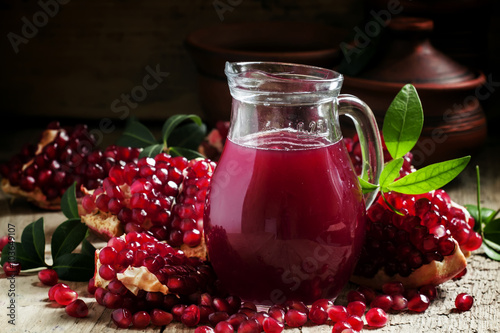 Jug with fresh pomegranate juice on the background of open grena photo