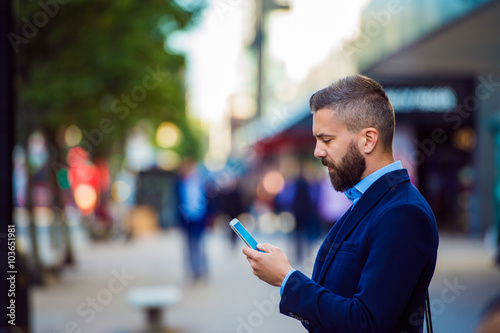 Hipster manager holding smartphone, texting outside in the stree photo